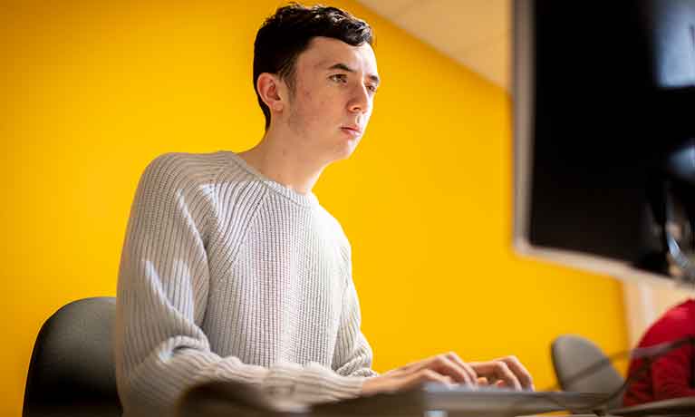 Man using a computer sitting on a yellow background