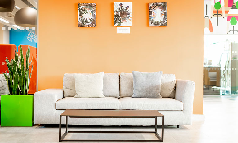 Sofa positioned against an orange walk with three photos and a coffee table