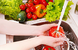 Arms and hands washing a vegetable in a sink with the tap running and other vegetables in the side