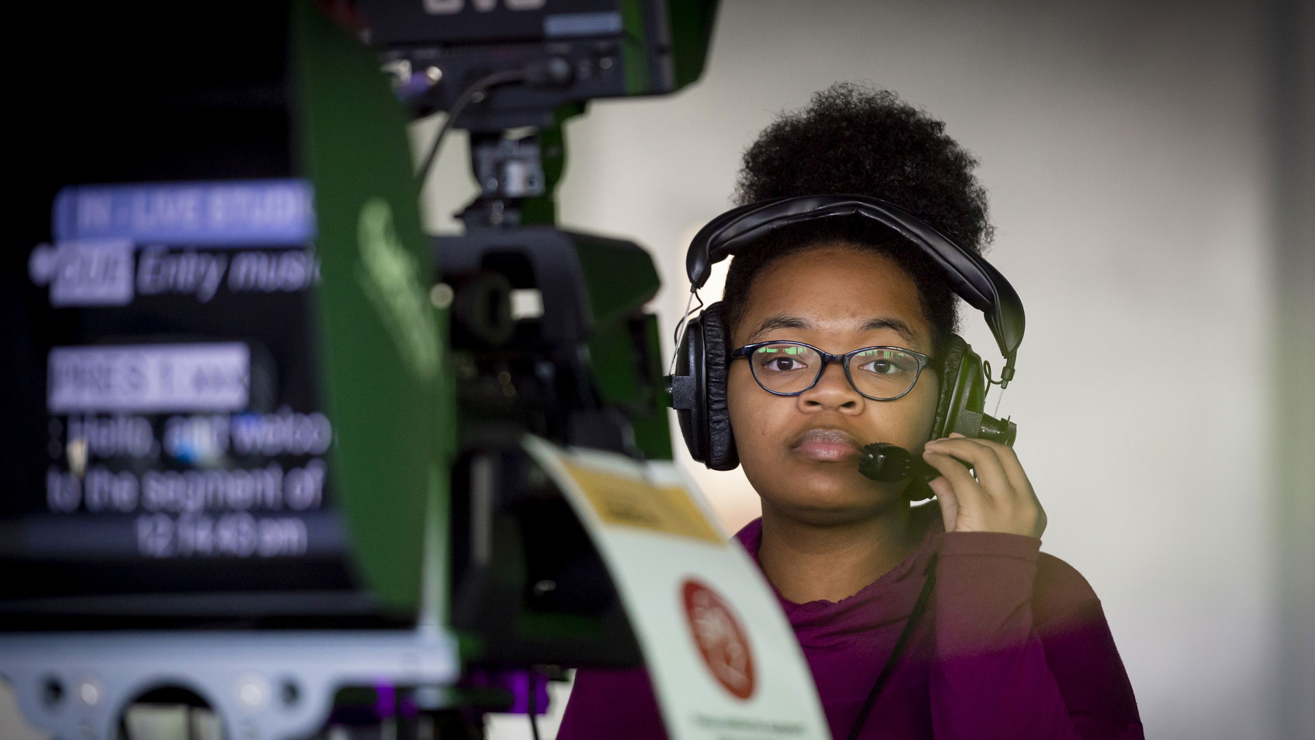 Student with a headset on in front of an autocue in the Media TV Tank