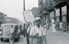 three men with picket boards walking down a street protesting with passers by in the background