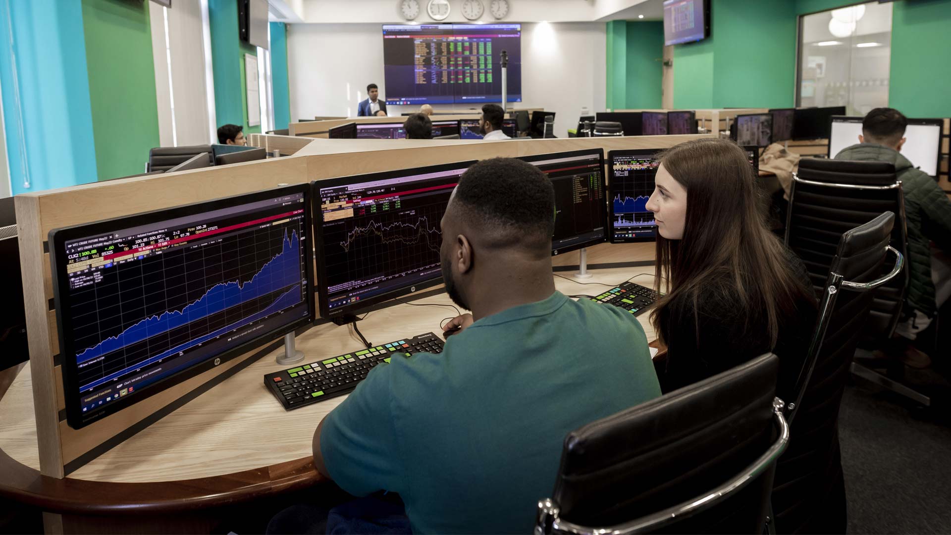 Two students in front of a bank of screens displaying financial data.