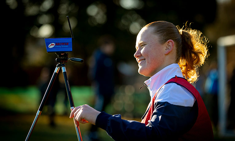 A smiling student holds a camera on a tripod
