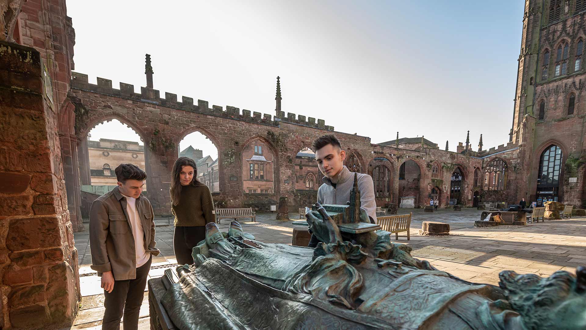 Three students studying a monument in the Coventry Cathedral ruins