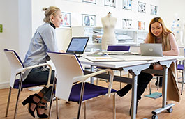Two women looking at designs on laptops in a bright studio