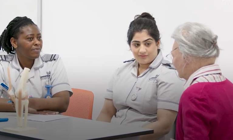 2 trainee nurses sitting at a table with an elderly patient