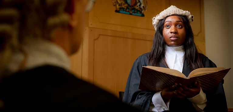 Student in law attire and wig holding a book in court