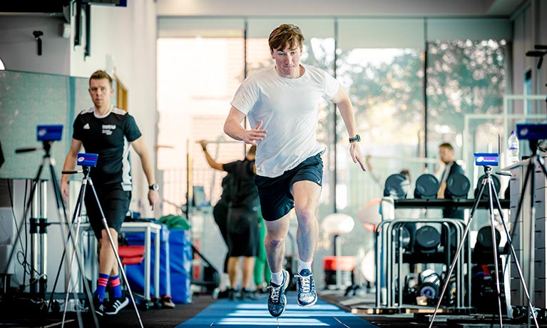 Young male running in a gym environment filled with people working out