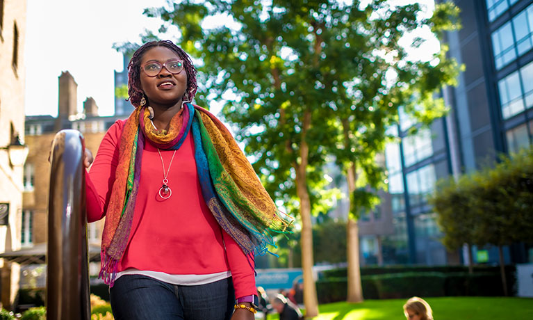 Student in a colourful jumper and scarf walking through the Coventry University London campus.