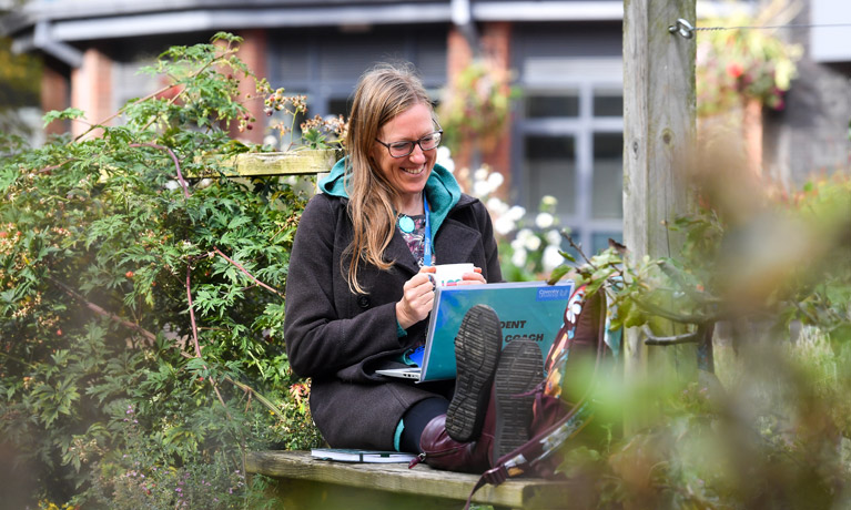 A member of staff in the edible garden, with her feet up and her laptop in her lap.