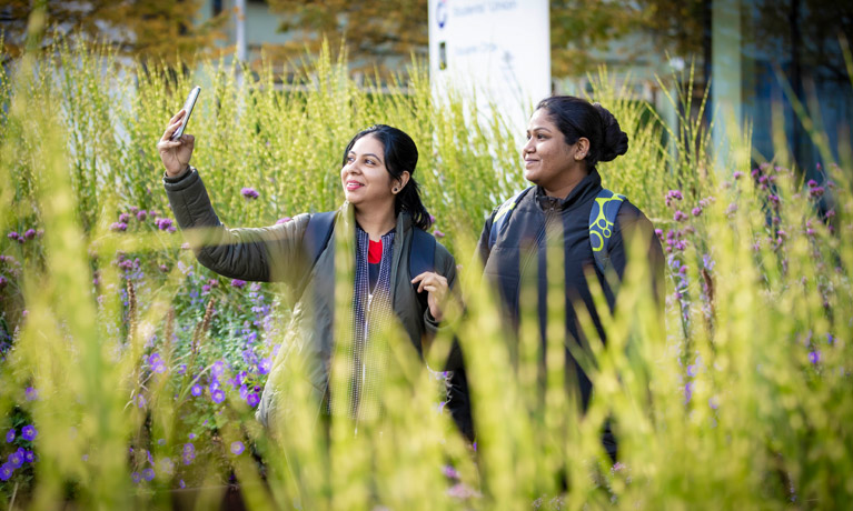 Two students in the garden by The Hub, taking a selfie in the tall lavender.