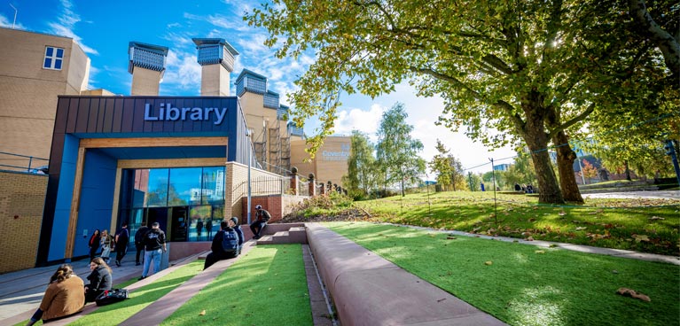 Lanchester Library entrance with students sitting on the tiered grass steps outside