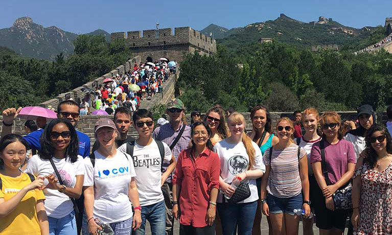A group of Confucius Institute language students smiling for the camera with the Great Wall of China behind them.