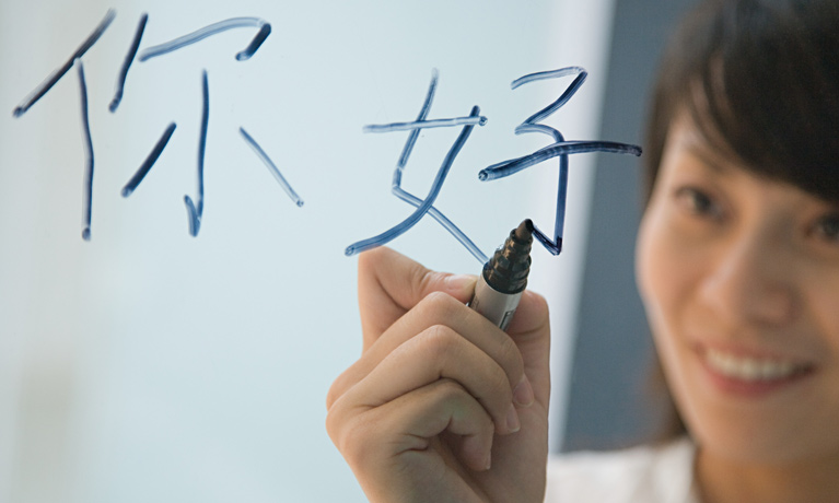 A Chinese woman writing 'hello' in Mandarin on a clear screen.