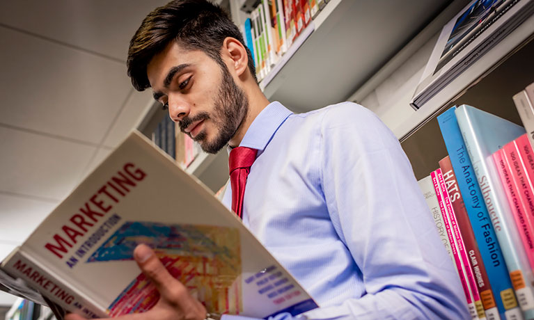 Male student reading a book in a library.