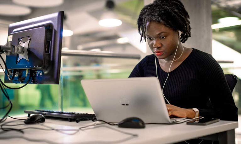 Female student wearing earbuds working on a laptop