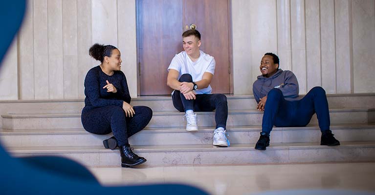 Three students on a flight of stairs inside a building talking