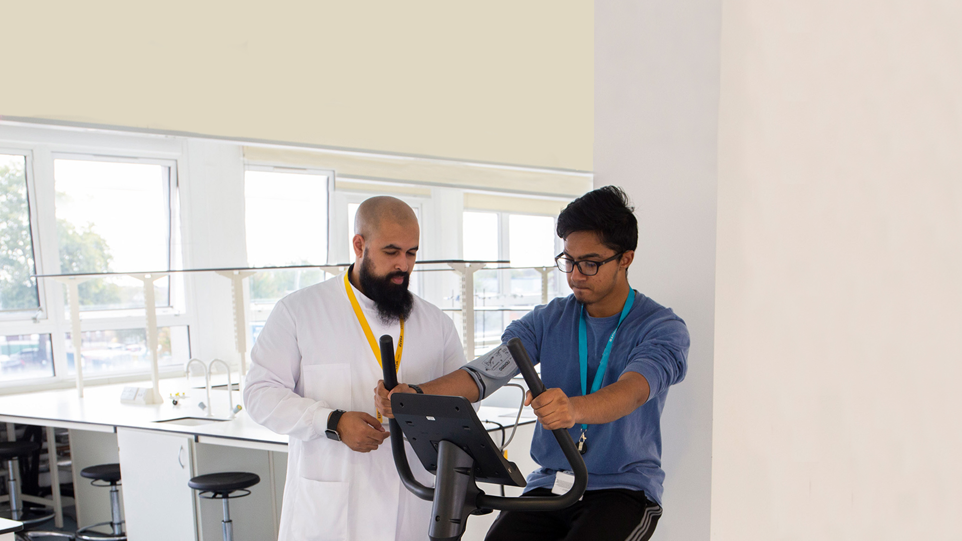 A Public Health student using an exercise bike for testing, with a tutor stood next to him.