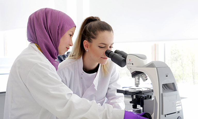 Two students looking through a microscope in a lab
