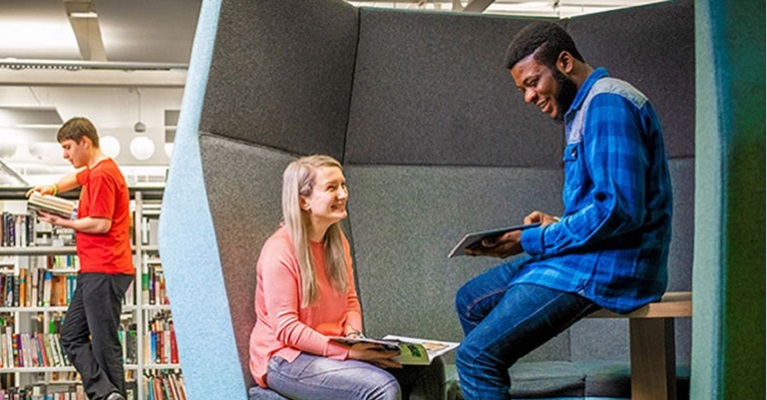Students sat in a pod in a library reading textbooks