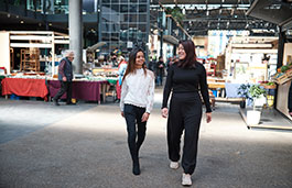 two females walking through an outdoor market with market stalls behind