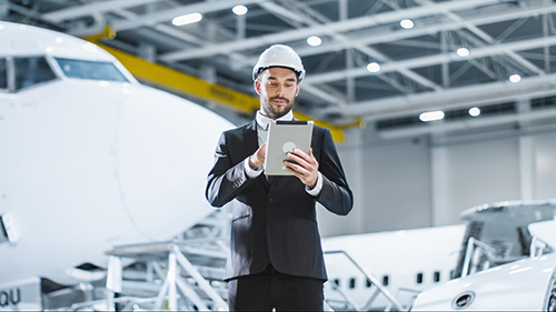 Aviation Management student in an airport hangar, using a tablet, in front of a plane