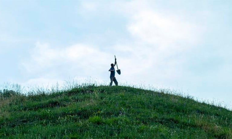 man walking on a hill with a spade