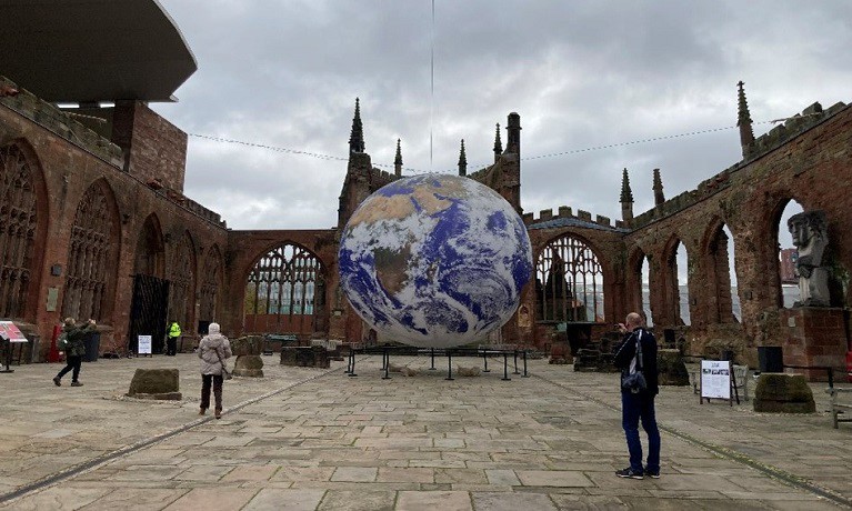 people walking through coventry cathedral with a hanging earth