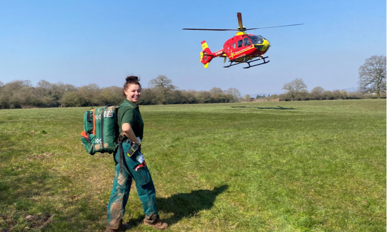 Student paramedic walking on a field with an air ambulance in the background
