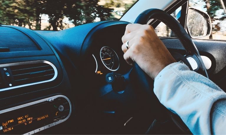 Person with hand on steering wheel with a car dashboard in focus