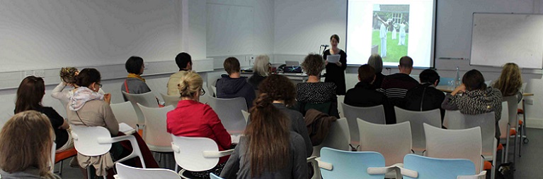 Female addresses room in front of big screen.
