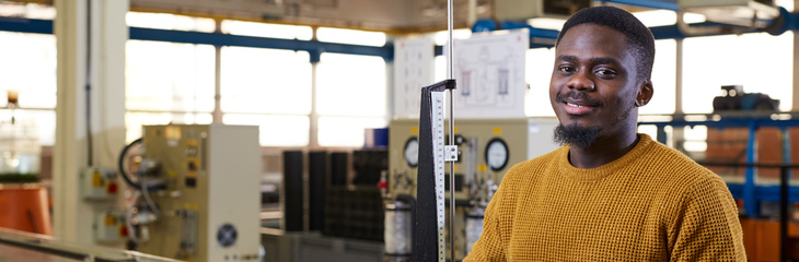 A student in a bright yellow jumper smiling in an engineering lab.