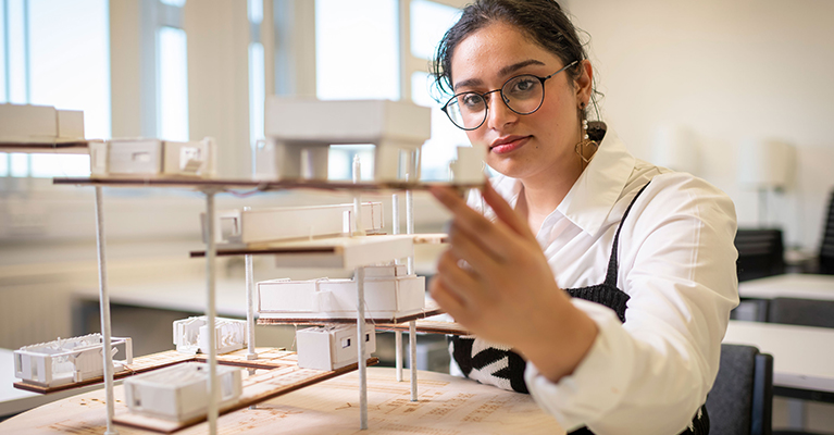 A student in a classroom sat at a desk with a art structure of a building on the table