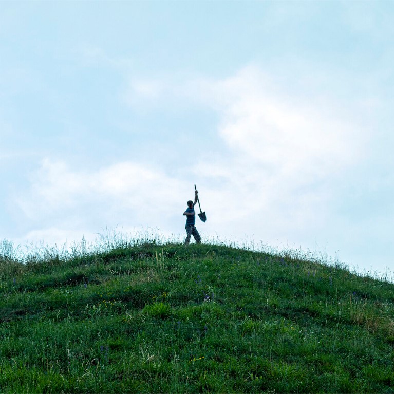 Person standing on a hill holding a spade