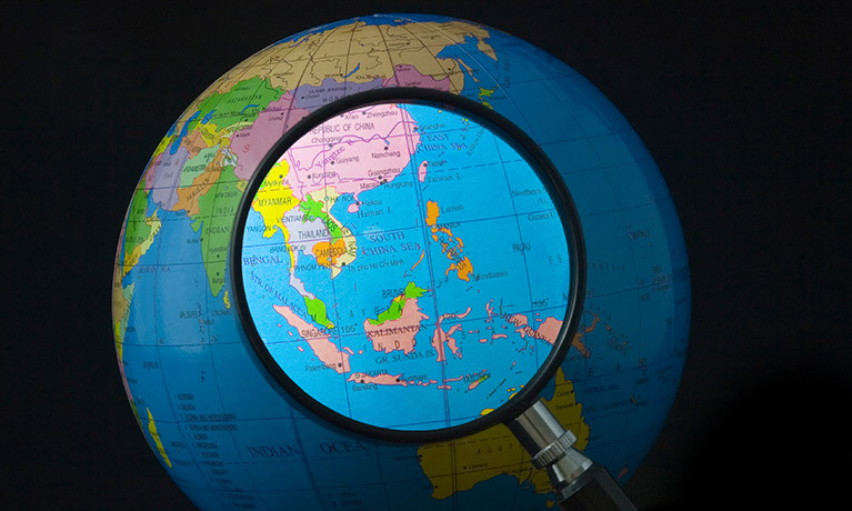 A globe with a magnifying glass illuminating Southeast Asia
