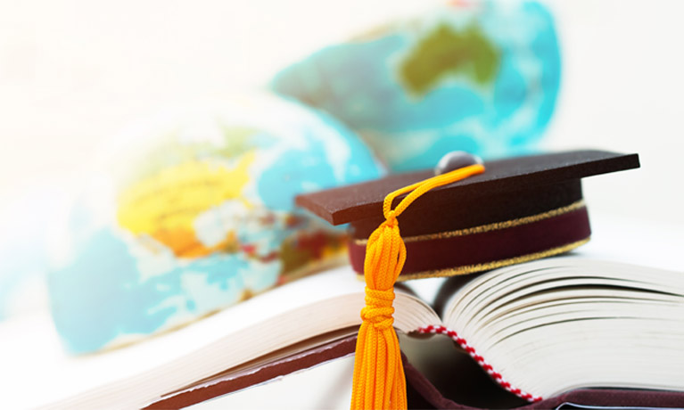 Graduate hat resting on open hardback book with globe in the background