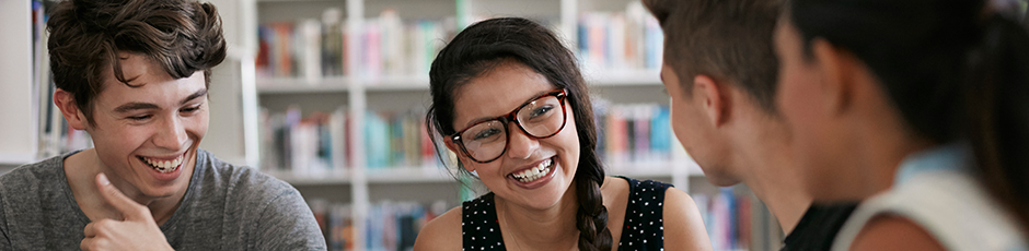 A close up of four students in a library smiling and talking with one another