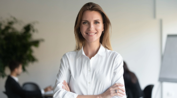 Smiling woman in a white shirt standing with arms crossed in an office.