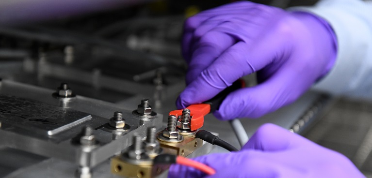 Closeup of hands wearing purple gloves using a mechanical tool to loosen up a screw