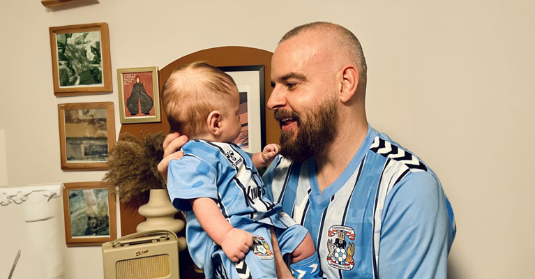 Dale Driver holding his baby in a Coventry City FC matching kits