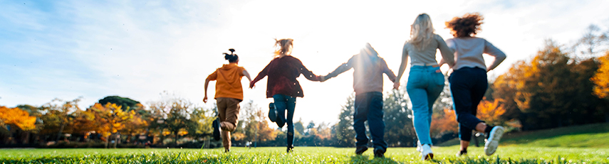 A racially diverse family running hand in hand away from the camera on a sunny autumn day