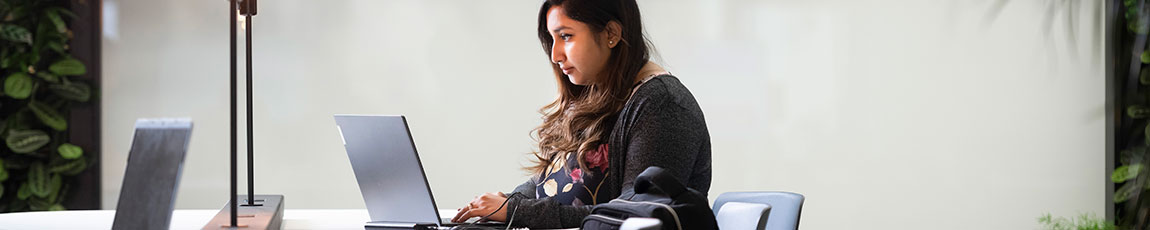 Female student sat at a desk working on her laptop