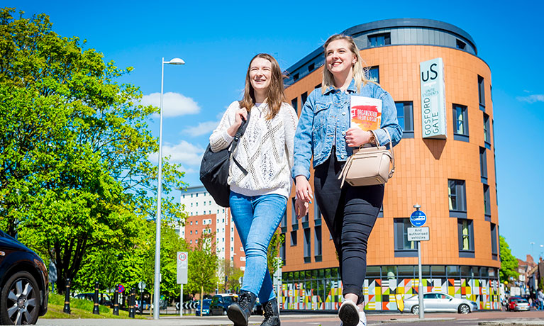 Two students walking past an accommodation block on a sunny day