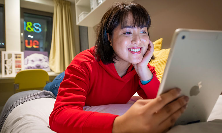 Smiling student lying on her bed looking at her laptop