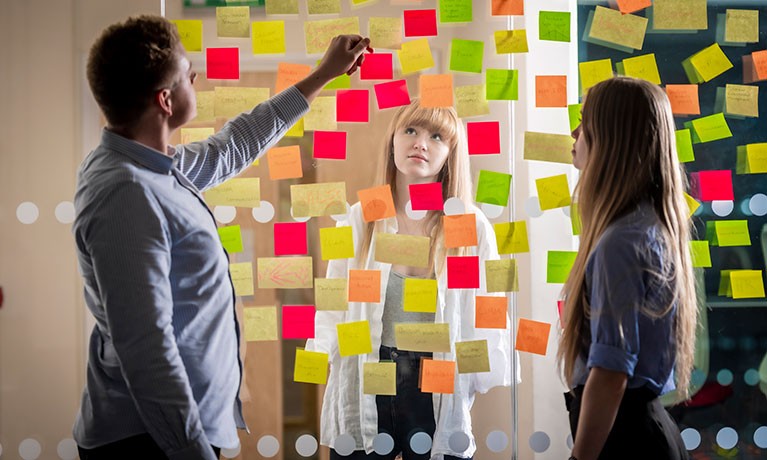 Students sticking coloured post-it notes on a transparent board