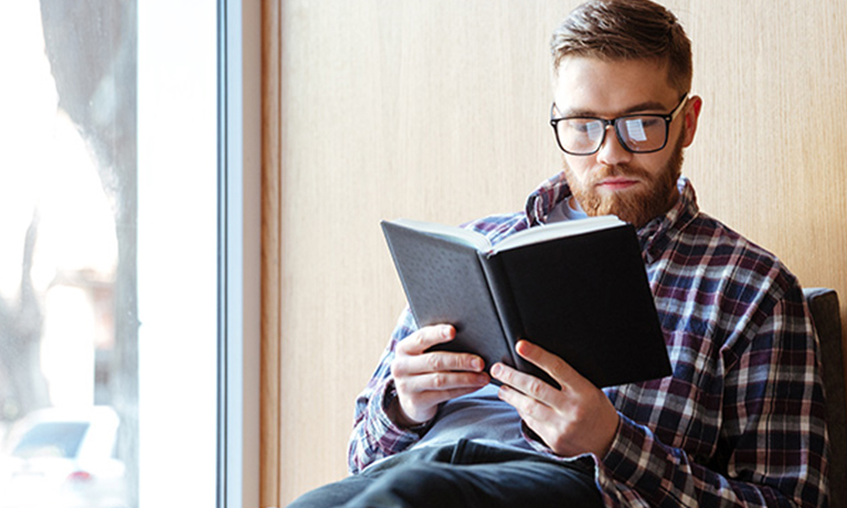 Coventry University student sat next to a window reading on campus