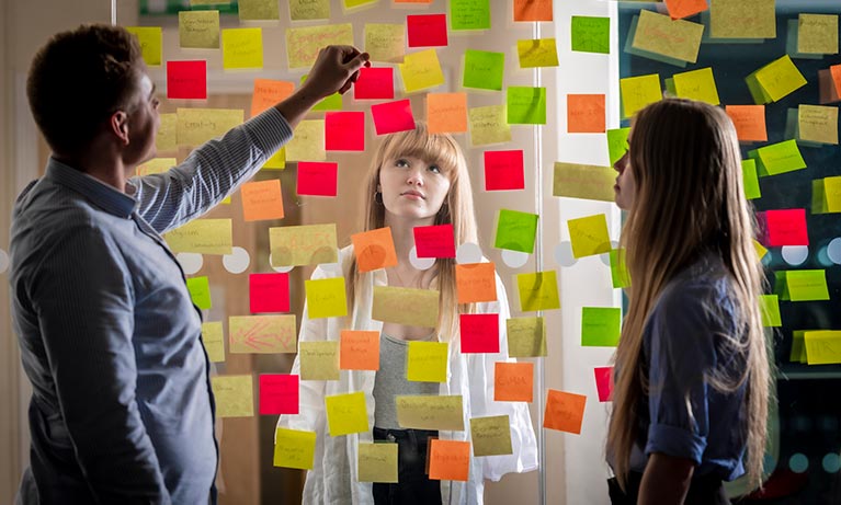 three people looking at a large transparent board with arranged postnotes