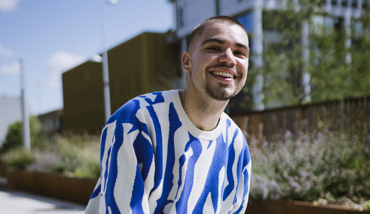 A portrait of a student wearing a blue patterened jumper smiling at the camera