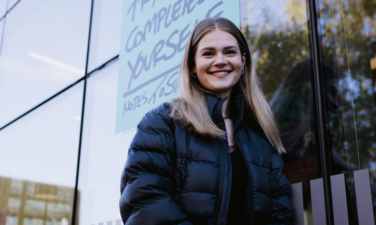 Smiling student leans against a glass wall