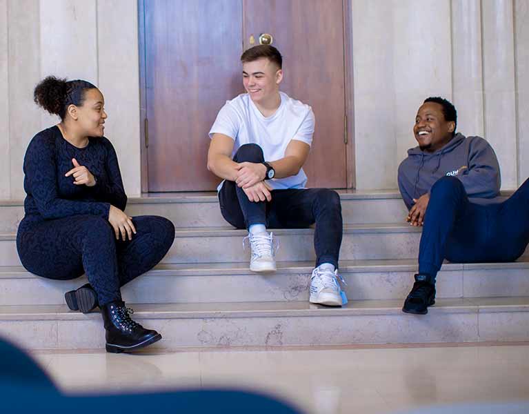 Three students sitting on external steps of a building